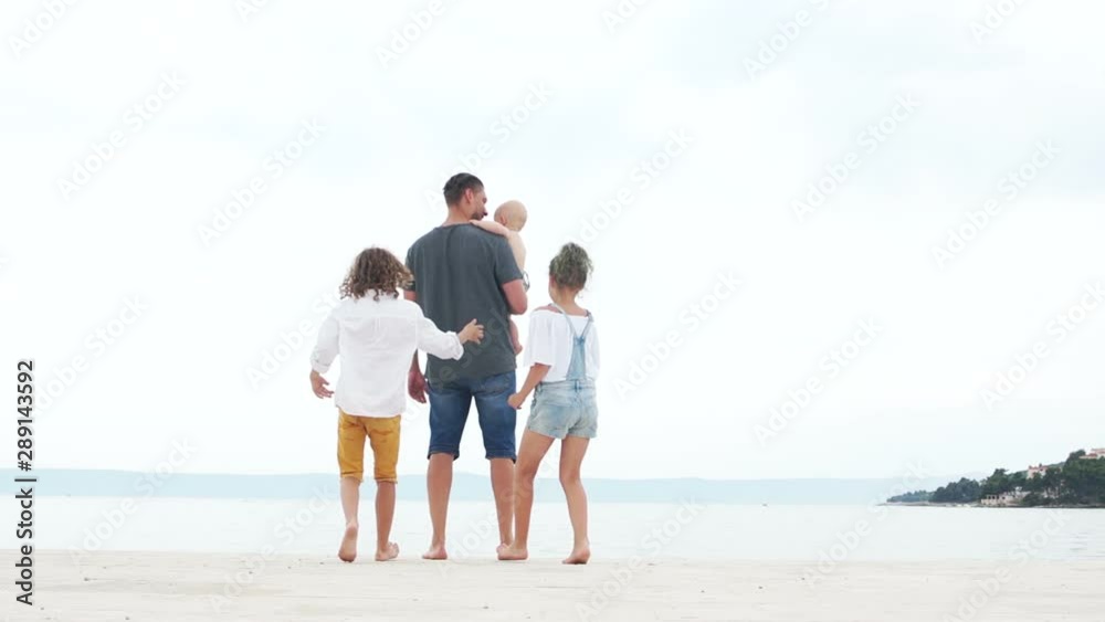 Young man with three children on the beach. The baby in the arms of his father and two teenagers, a boy and a girl. Lonely father, fathers day Young man with three children on the beach. The baby in the arms of his father and two teenagers, a boy and a girl. Lonely father, fathers day