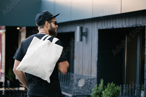 Young man holding white textile eco bag against urban city background. Ecology or environment protection concept. White eco bag for mock up. photo