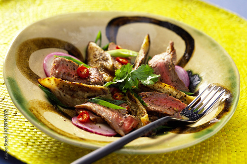Succulent Thin strips of chillie Beef fillet with garnish. In rustic bowl with fork
