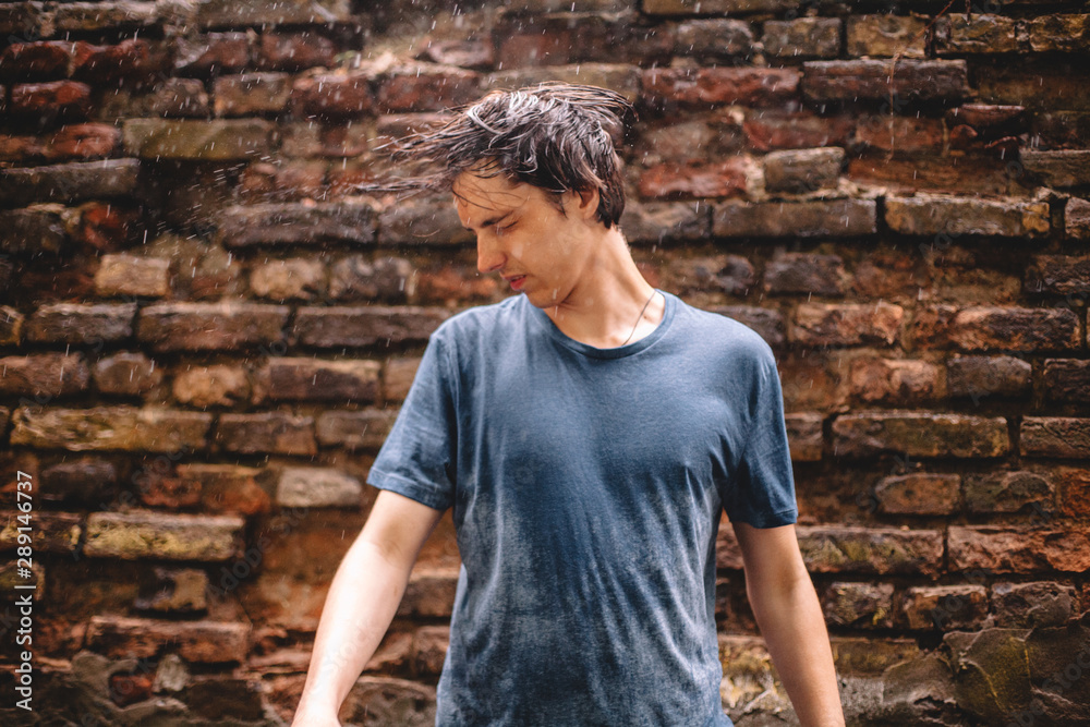 Young man tossing hair standing in the rain against brick wall