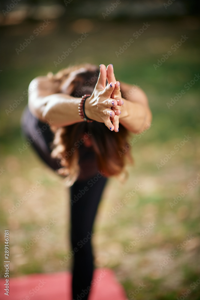 Focused Caucasain woman standing in Warrior III yoga pose. Nature exterior. Selective focus on hands. Focused Caucasain woman standing in Warrior III yoga pose. Nature exterior. Selective focus on hands.