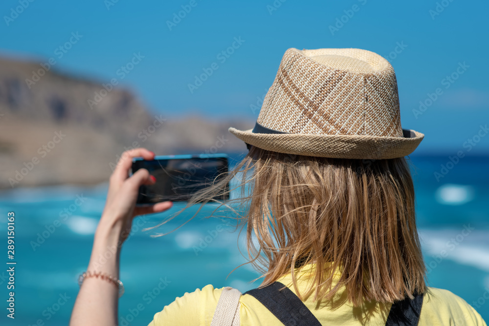 Technology, summer holidays, travel and people concept - happy young woman in  sun hat taking photo with smartphone over beach background - Image.