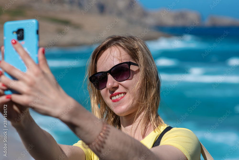 The young blondie girl is talking selfie against picturesque sea view during her holidays in Spain.