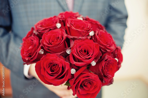 man in a suit holds a bouquet of red roses close-up.