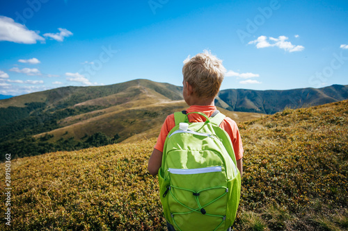 Little boy with backpack standing on top of mountain