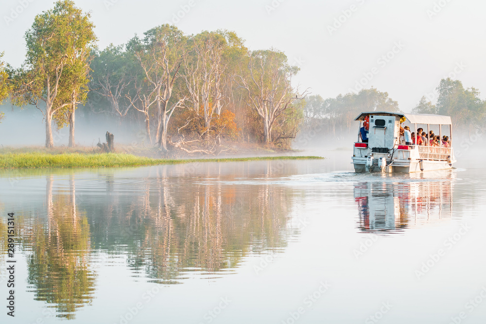 A boat of the Yellow Water Cruise floats in the morning mist on the billabong at sunrise, Kakadu National Park, Northern Territory, Australia