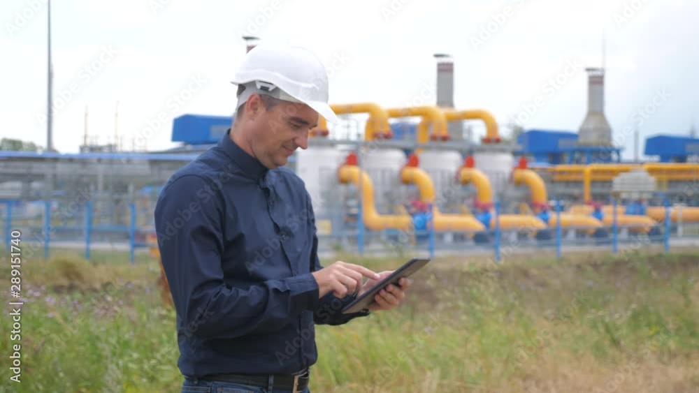 teamwork gas production station concept. Engineering man standing writes documents on digital tablet white safety helmet. man engineer in helmet work lifestyle at the station are studying on gas teamwork gas production station concept. Engineering man standing writes documents on digital tablet white safety helmet. man engineer in helmet work lifestyle at the station are studying on gas