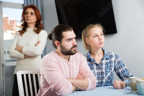 Upset mature woman talking with sad daughter and her boyfriend at home