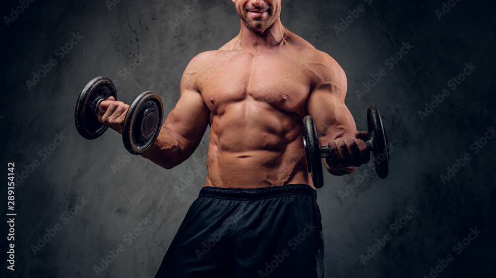 Happy smiling bodybuilder is doing exercises with barbels and showing his muscules on the dark background.