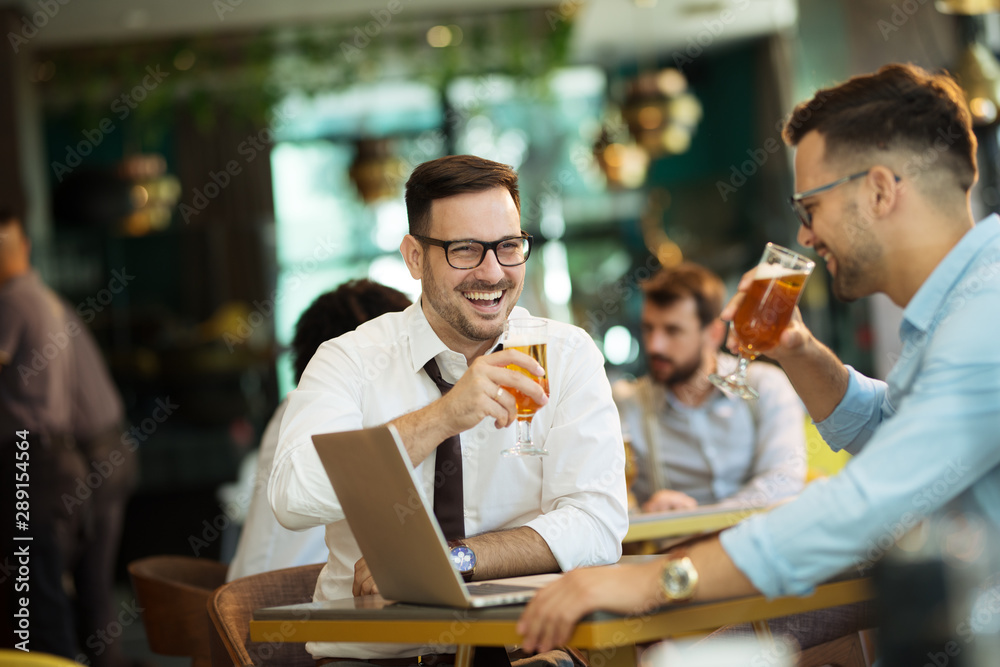 Obraz premium Two young businessmen use a laptop and drink beer