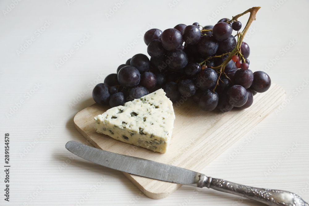 Red wine in an elegant glass, cheese and a bunch of grapes.
