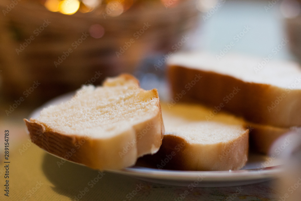 Loaf of white bread, sliced in a plate on a table on a blurry brown background. Close-up.