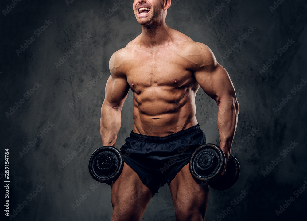 Happy joyful bodybuilder is doing exercises with barbels and showing his muscules on the dark background.
