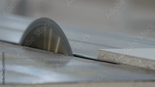 An employee of a furniture factory on a machine with a circular saw cuts in half a white sheet of chipboard. Close-up. Selective focus. Joiner's shop. Video with the sound of a sawing tool.