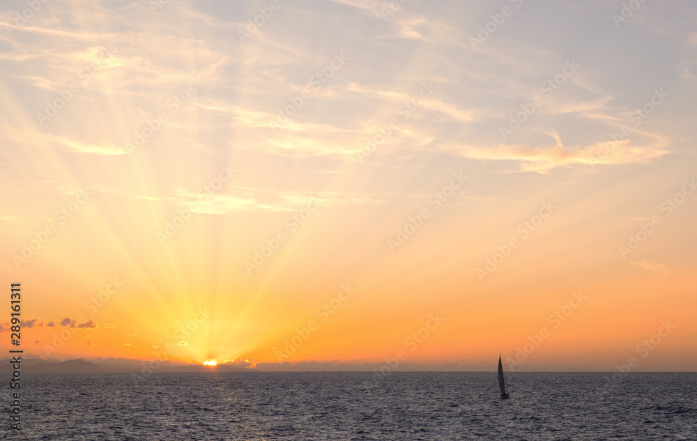 Sun rays at sunset with sailboat on the coast of Donostia, Cantabrico Sea, Euskadi