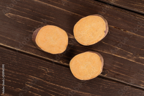 Fototapeta Naklejka Na Ścianę i Meble -  Group of three slices of fresh brown sweet potato flatlay on brown wood