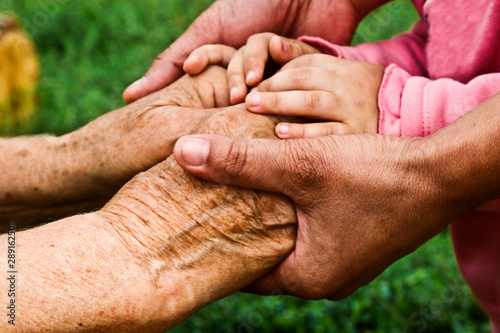 Old hands of a grandmother, daughter and a small child