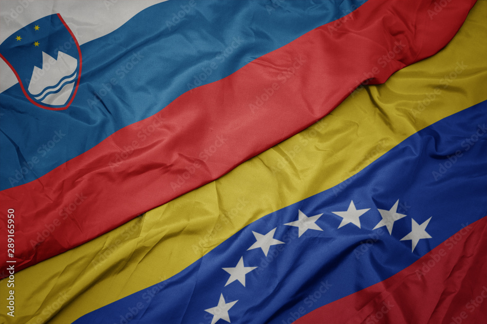 waving colorful flag of venezuela and national flag of slovenia.