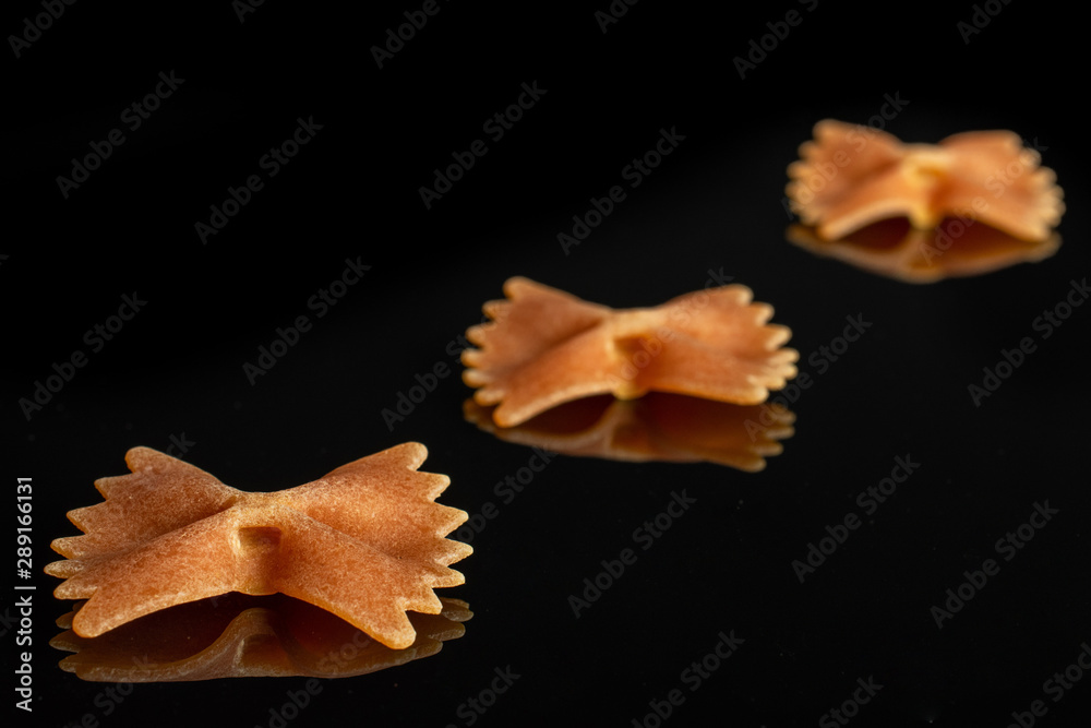 Group of three whole red uncooked farfalle isolated on black glass