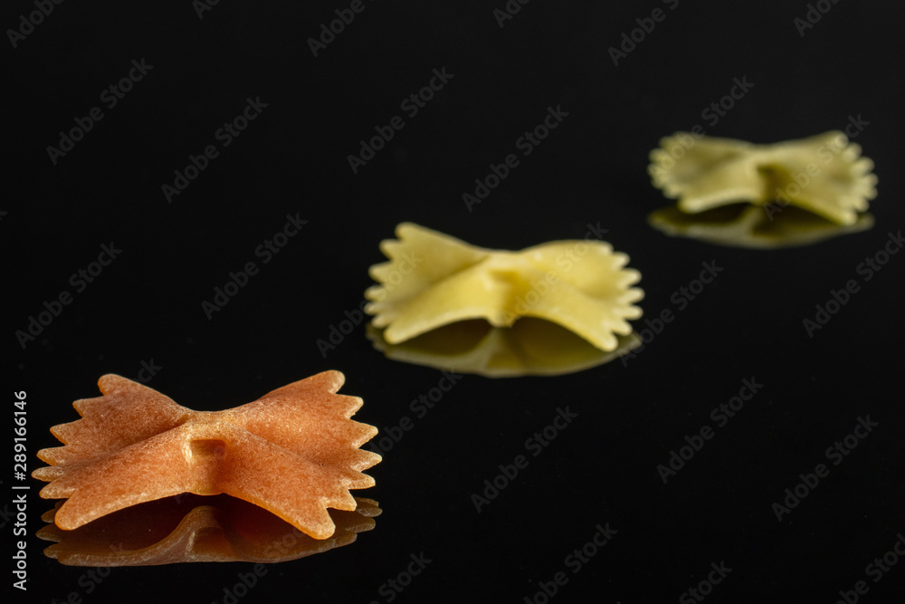 Group of three whole red, yellow and green uncooked farfalle isolated on black glass Group of three whole red, yellow and green uncooked farfalle isolated on black glass