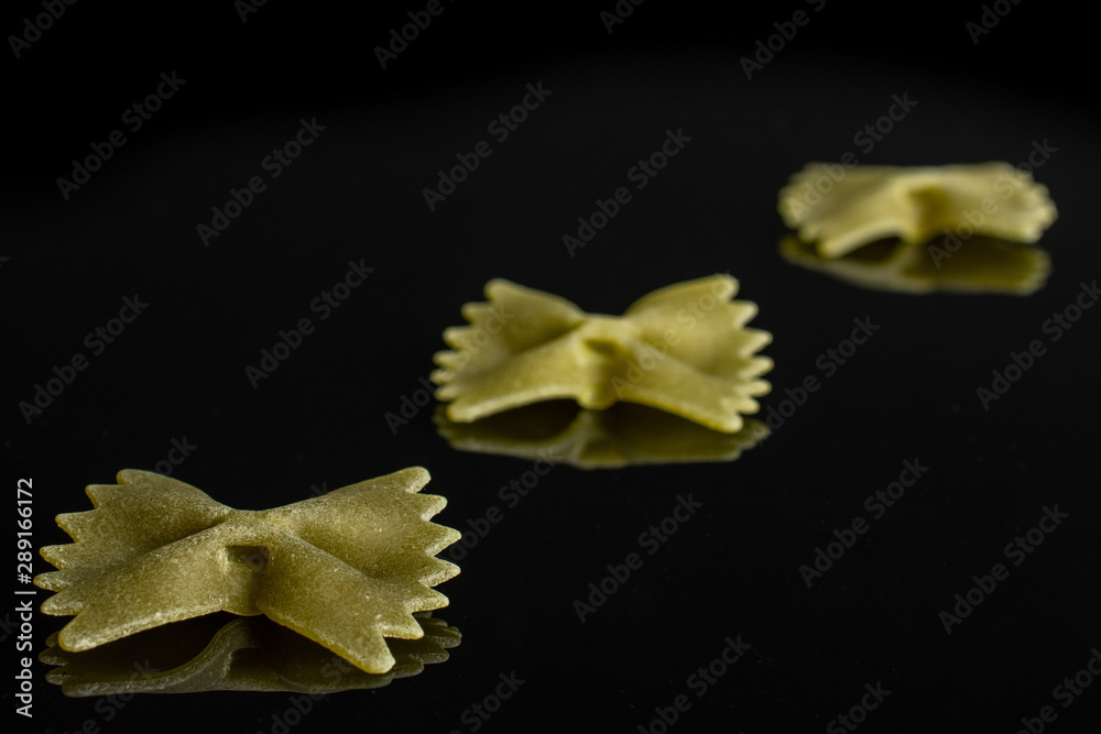 Group of three whole green uncooked farfalle isolated on black glass