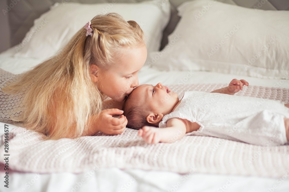 Young beautiful mother holds a baby. Little sister kisses her little sister. Baby. Children bedroom. Young beautiful mother holds a baby. Little sister kisses her little sister. Baby. Children bedroom.