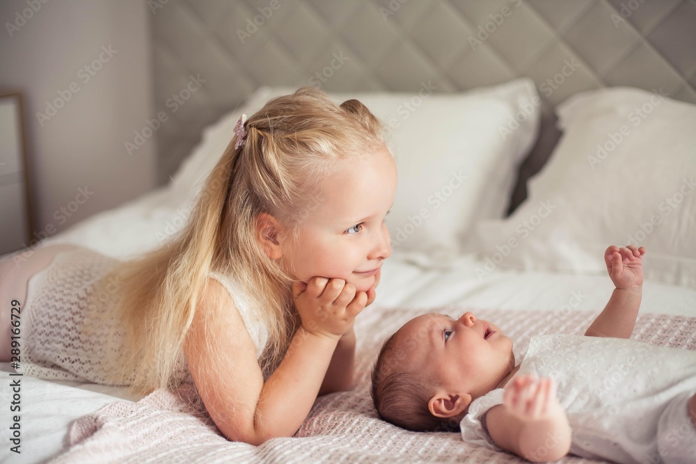 Young beautiful mother holds a baby. Little sister kisses her little sister. Baby. Children bedroom. Young beautiful mother holds a baby. Little sister kisses her little sister. Baby. Children bedroom.