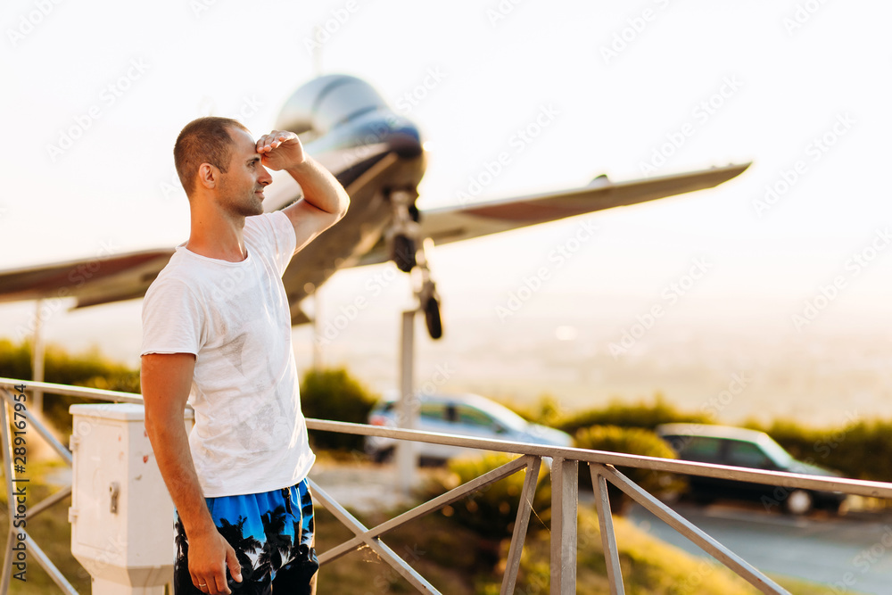 Cute guy looking away. Traveler stands on airplane background Cute guy looking away. Traveler stands on airplane background