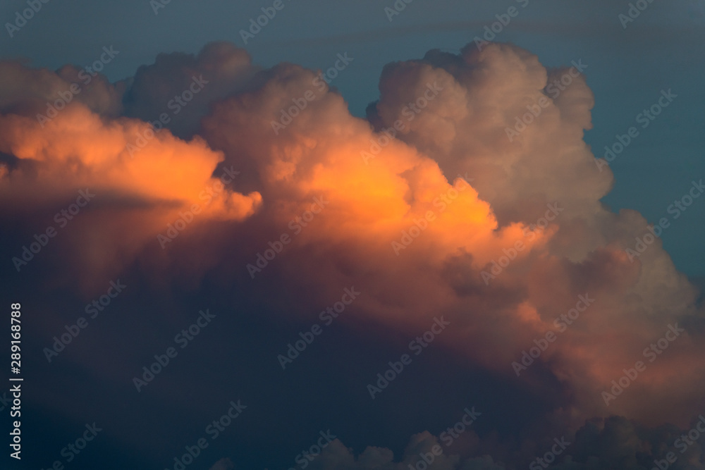 Cloudscape of fluffy storm clouds illuminated in hues of yellow, orange, pink, and purple by the light of sunset Cloudscape of fluffy storm clouds illuminated in hues of yellow, orange, pink, and purple by the light of sunset