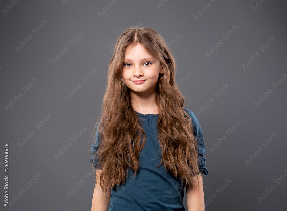 Fototapeta premium Happy excited positive kid girl with long hair on grey background with empty copy space. Closeup
