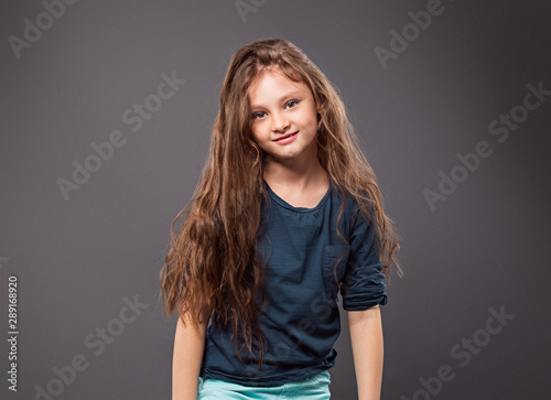 Happy excited positive kid girl with long hair on grey background with empty copy space. Closeup