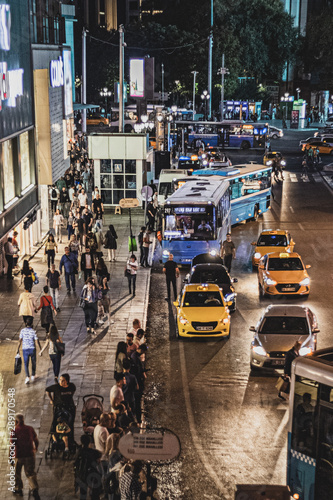 People who are out of work and waiting for a bus in the crowd of the city and the traffic flowing by them, buses, taxis, people, night lights of the city