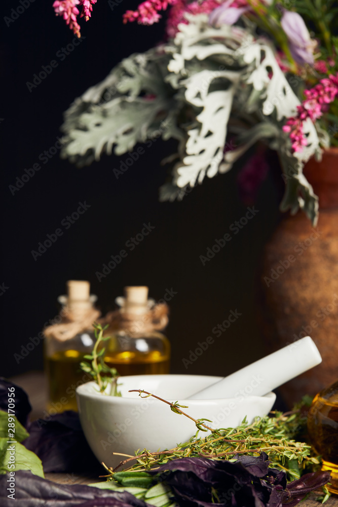white mortar with pestle near bottles and vase with fresh flowers on wooden surface isolated on black white mortar with pestle near bottles and vase with fresh flowers on wooden surface isolated on black