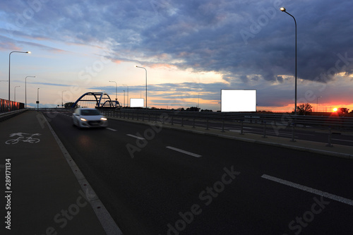 Fototapeta Naklejka Na Ścianę i Meble -  Samochód osbowy na drodze, zachód słońca, bilbord reklamowy, tekst, wiadukt, most.	