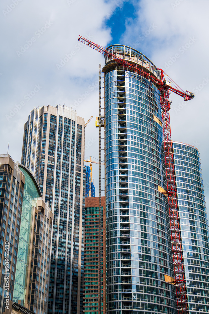 Construction of modern glass and steel high rise office and residential buildings with red and yellow cranes
