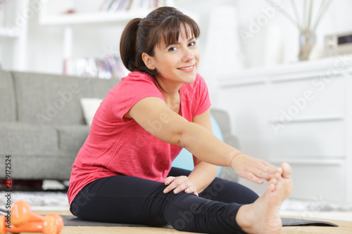 young woman stretching legs on fitness mat at home