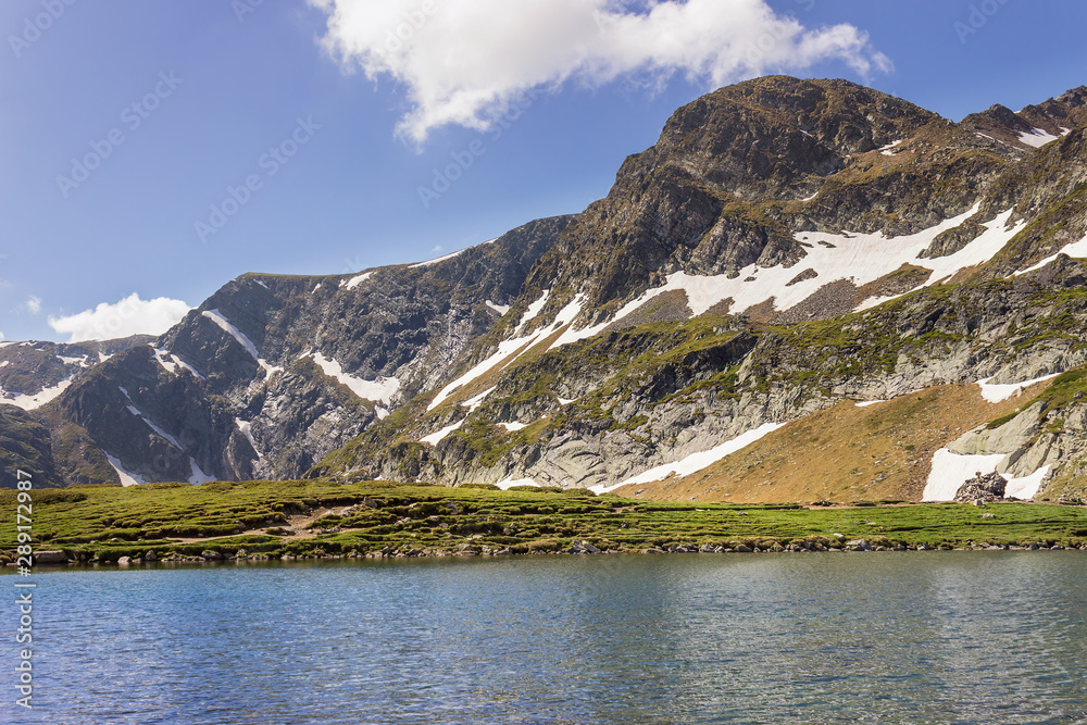 Scenic view across famous Kidney lake on Rila mountain in Bulgaria on snow covered rocky cliffs under a blue sky