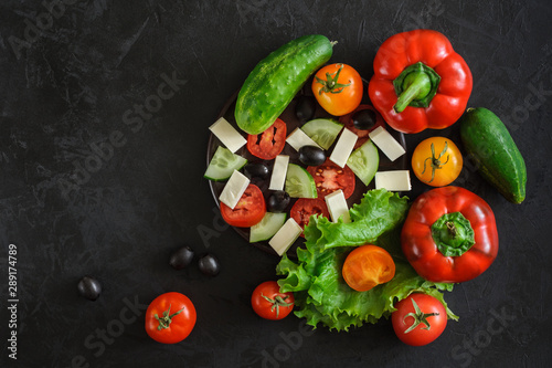 top view of a set of fresh vegetables for a greek salad whole and sliced ??on a black concrete background. creative template with space for text, logo, slogan or advertisement