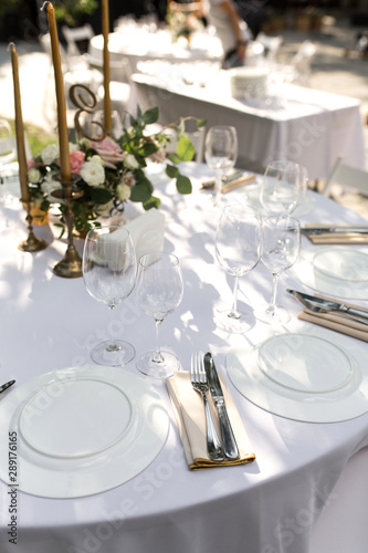 Wedding table setting decorated with fresh flowers in a brass vase. Wedding floristry. Banquet table for guests outdoors with a view of green nature. Bouquet with roses, eustoma and eucalyptus leaves