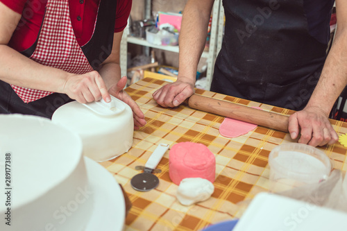Schilderij op canvas Female chef in red work wear in pasty shop fixing fondant on white fondant cake