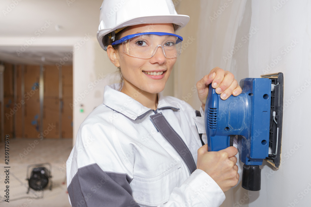 portrait of professional female worker using sander on interior wall portrait of professional female worker using sander on interior wall