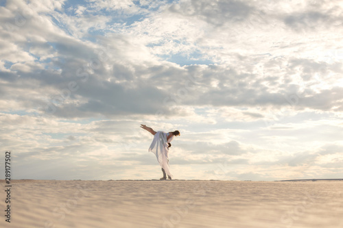 Romantic couple dancing in sand desert. The guy lifts the girl above himself. Sunset sky.