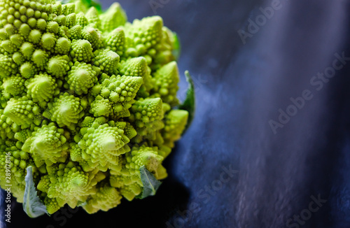 Close up view of amazing Romanesco broccoli or Roman cauliflower on wet dark blue background. Its form is a natural approximation of a fractal.