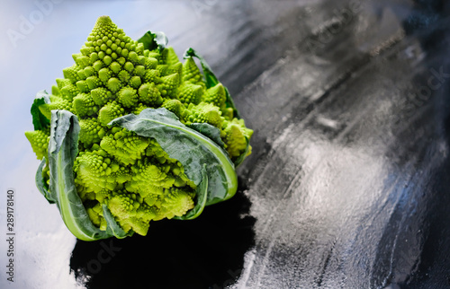 Amazing fresh green Romanesco broccoli or Roman cauliflower on wet dark background. Its form is a natural approximation of a fractal. Close up view.