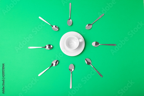 Flat lay composition of empty cup and new teaspoons on green background