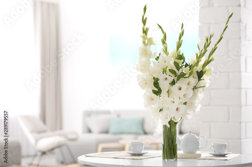 Foto Vase with beautiful white gladiolus flowers on wooden table in living room