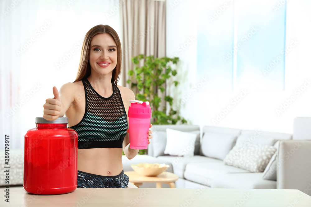 Young woman with bottle of protein shake at home. Space for text