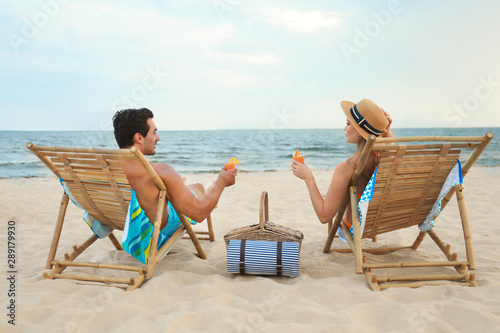 Happy young couple with cocktails sitting on deck chairs at sea beach