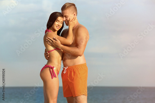 Young woman in bikini spending time with her boyfriend on beach. Lovely couple