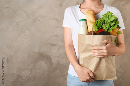 Woman holding shopping paper bag with different groceries against brown background. Space for text